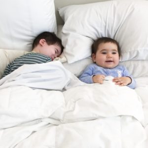having second child: brother and baby sister next to each other in parent's bed