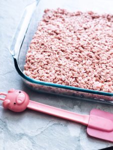 pink Krispie Treats in glass dish with pink spatula on counter