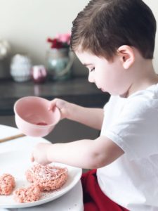 toddler decorating pink valentine heart-shaped rice krispie treat with sugar sprinkles
