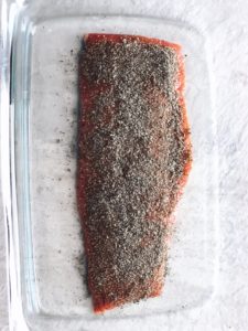 slab of salmon covered in seasoning in glass dish